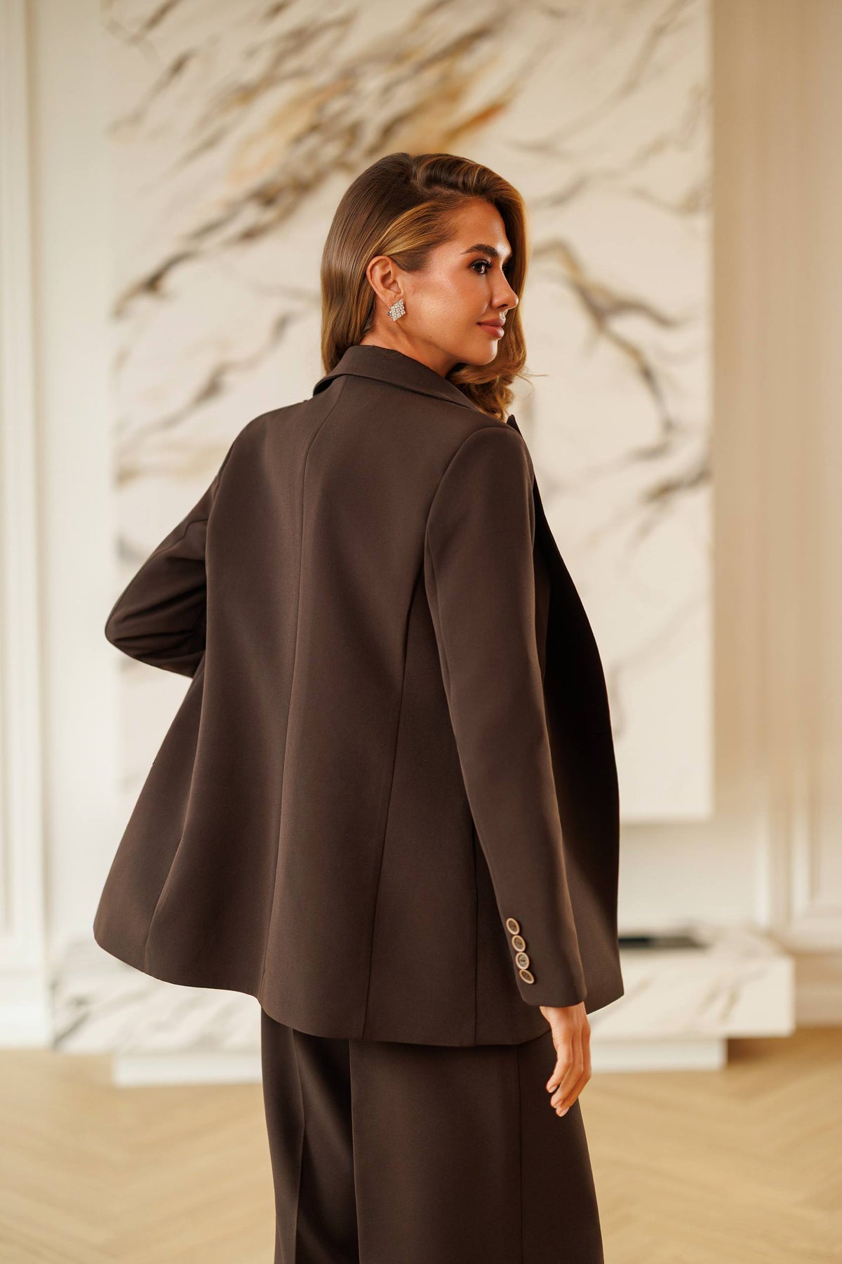 Woman wearing a brown suit standing in a room with marble walls.