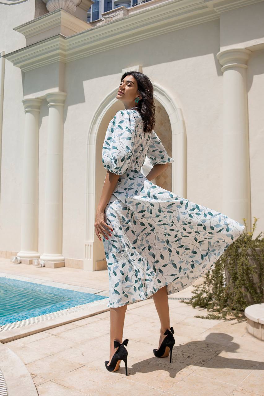 Woman in a floral dress standing by a pool with classical architecture in the background