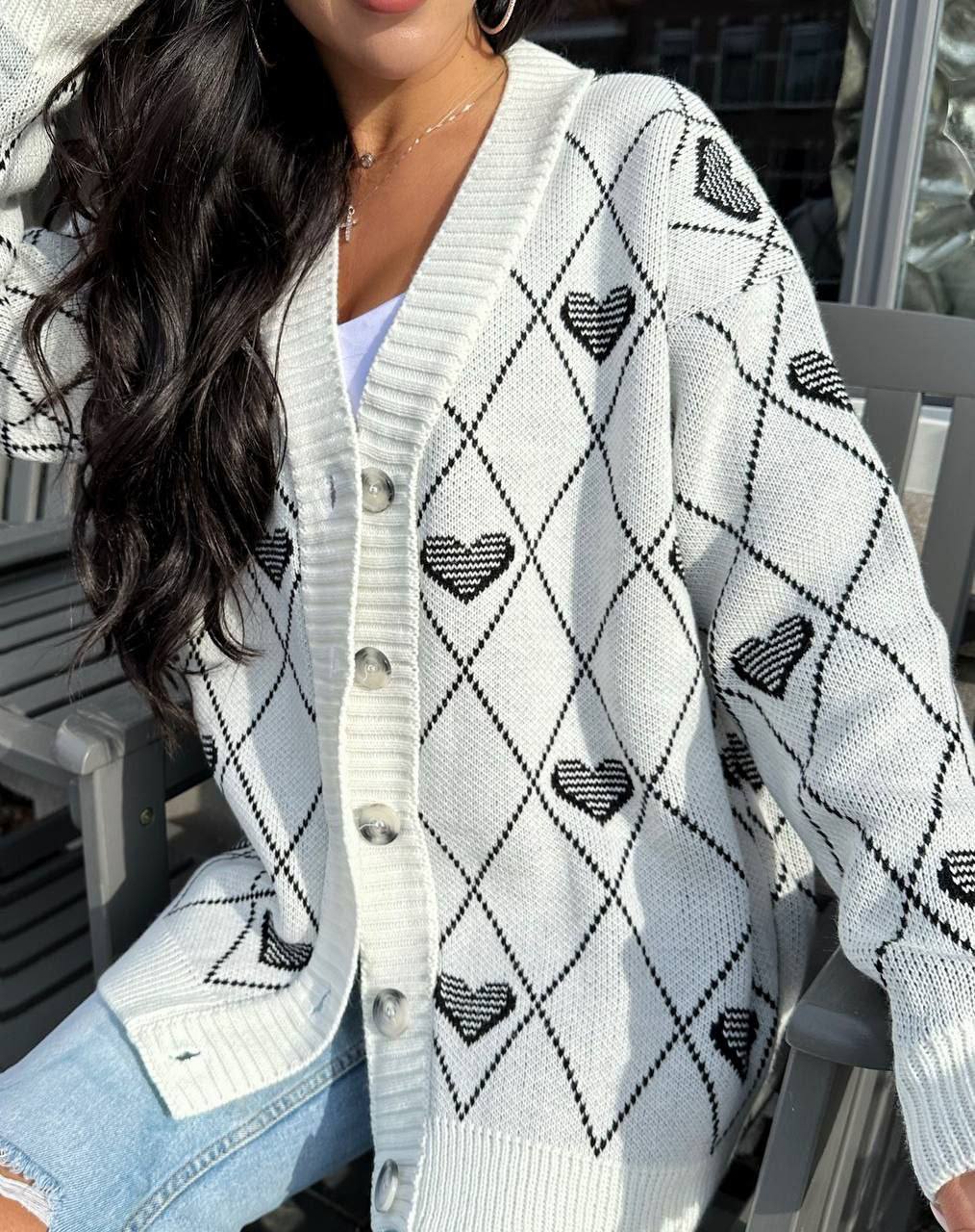 White cardigan with black heart patterns worn by a person sitting outdoors.