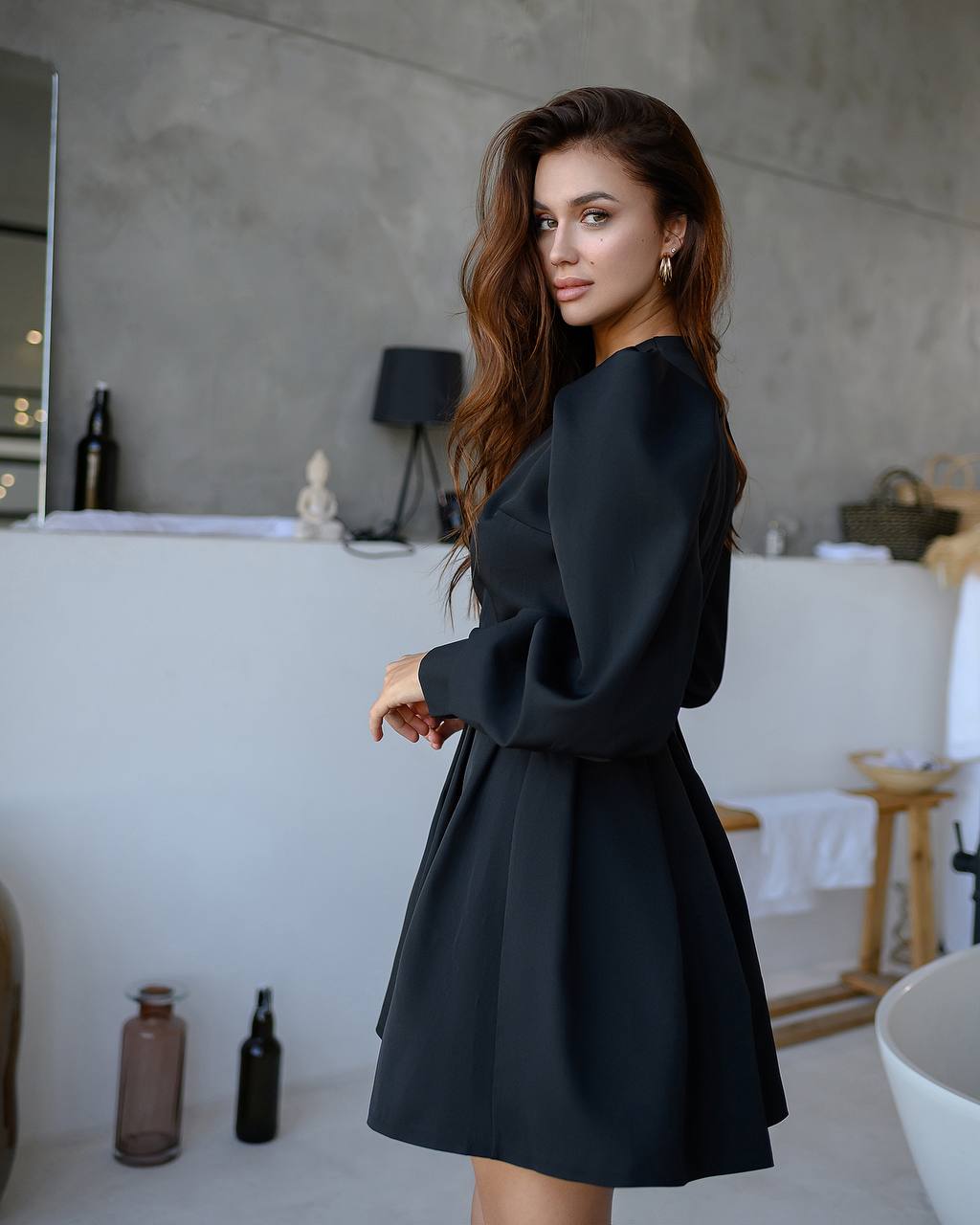 Woman in a black dress standing in a modern bathroom.