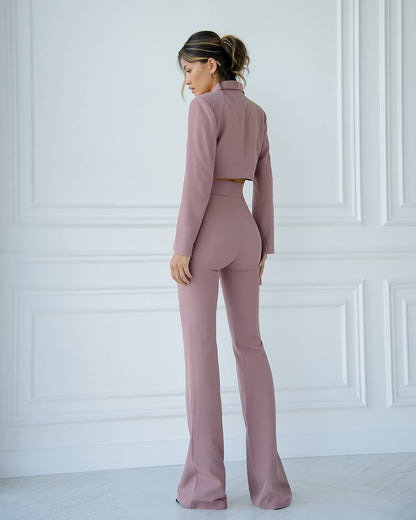 Woman wearing a pink suit standing against a white paneled wall.