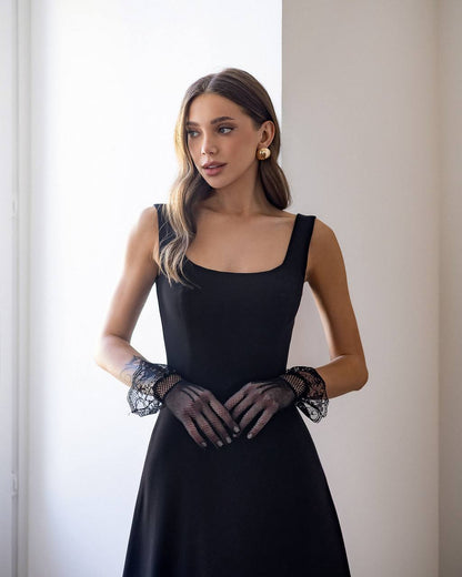 Woman wearing a black dress with sheer sleeves and gloves against a neutral background