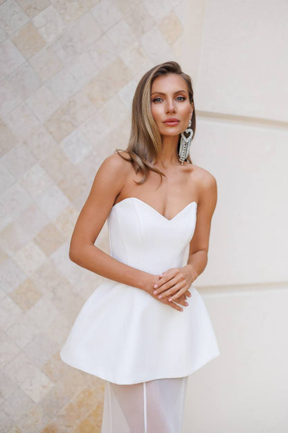 Woman wearing a strapless white dress with a textured beige wall background