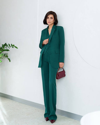 Woman in a green suit holding a red handbag against a white wall.