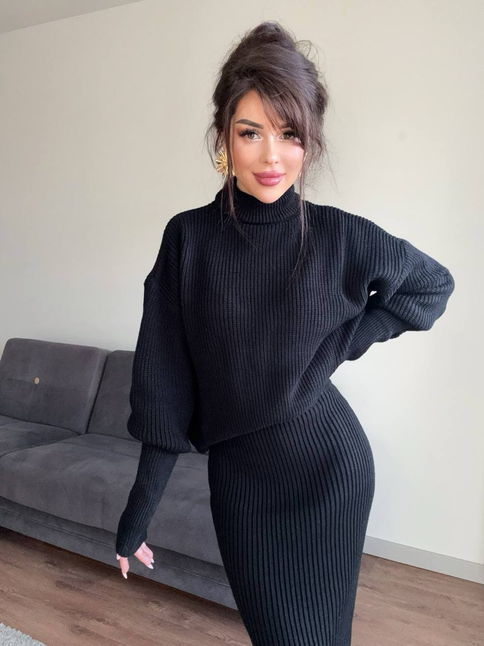 Woman wearing a black ribbed sweater and skirt in a room with a gray couch.