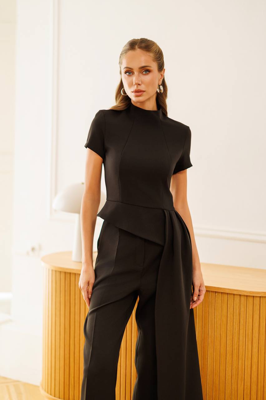 Woman wearing a black peplum top and high-waisted pants against a neutral background