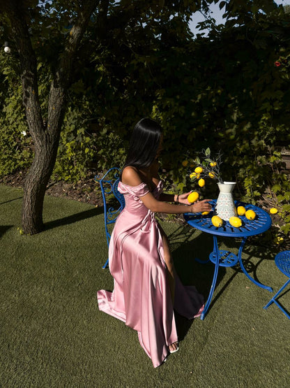 Woman in a pink dress standing next to a table with lemons and a vase outdoors.