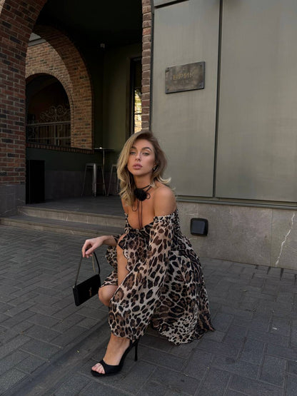 Woman in a leopard print dress sitting on a street corner.