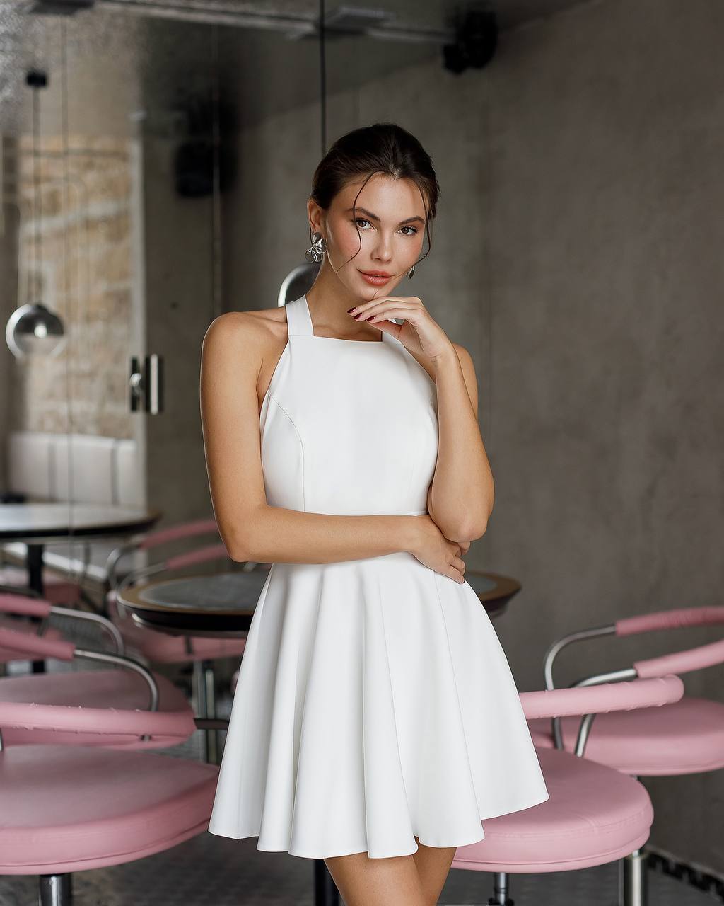 Woman in a white dress standing in a modern cafe with pink chairs.