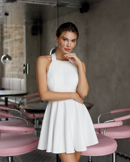 Woman in a white dress standing in a modern cafe with pink chairs.
