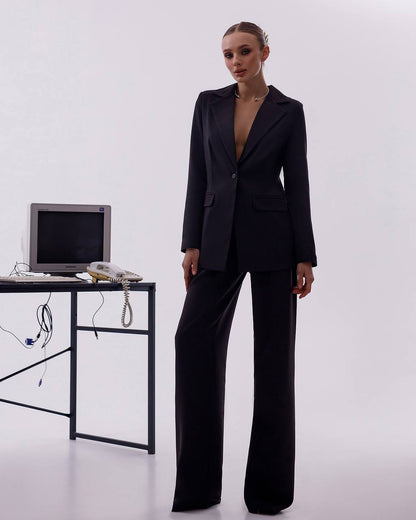 Person wearing a black suit standing next to a desk with electronic equipment on a white background