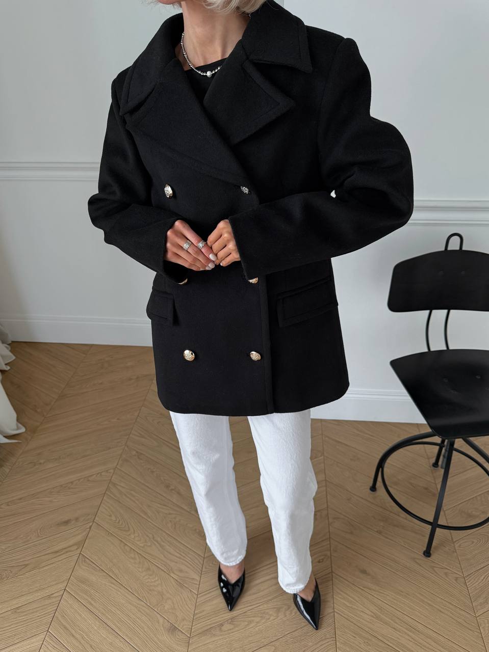 Person wearing a black coat with gold buttons in an indoor setting