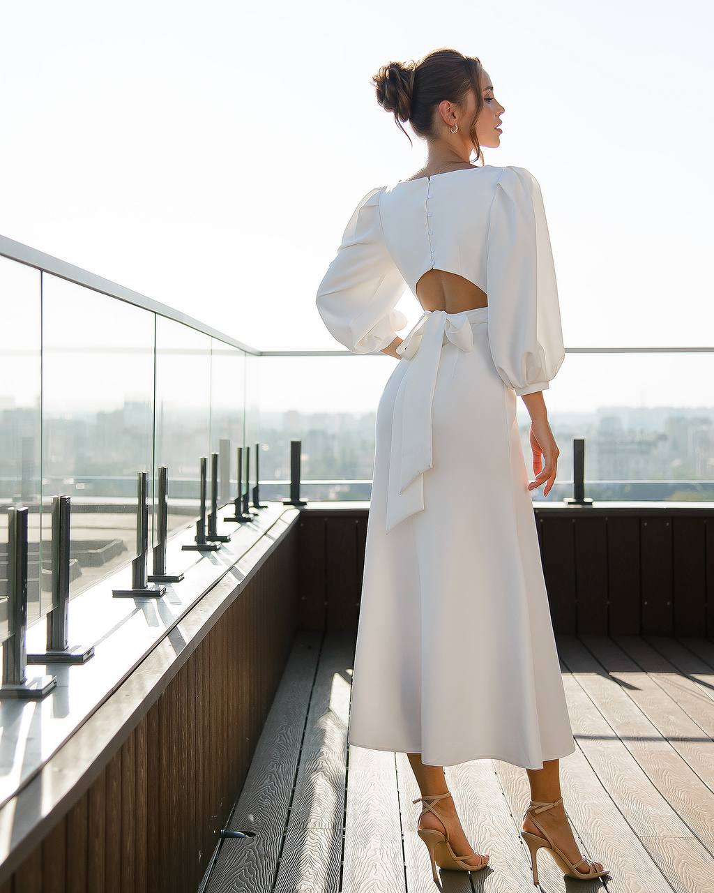 Woman in a white dress standing on a rooftop with a cityscape view.