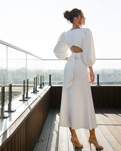 Woman in a white dress standing on a rooftop with a cityscape view.