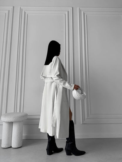Person wearing a white coat holding a helmet against a gray paneled wall.
