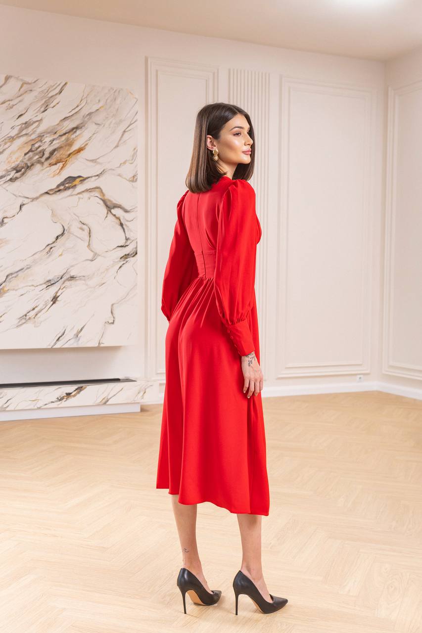 Woman in a red dress standing in a room with marble wall and wooden floor.