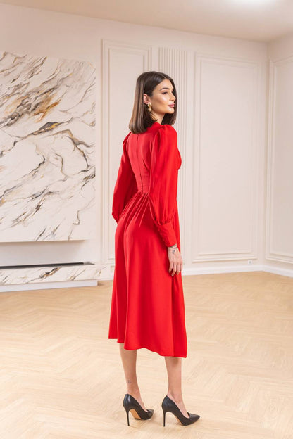 Woman in a red dress standing in a room with marble wall and wooden floor.