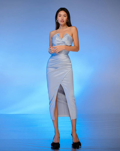 Woman in a light blue strapless dress with a slit on a blue gradient background