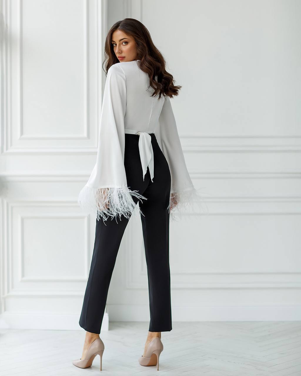 Woman wearing a white blouse and black pants against a white wall