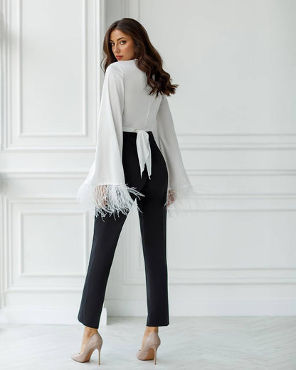 Woman wearing a white blouse and black pants against a white wall