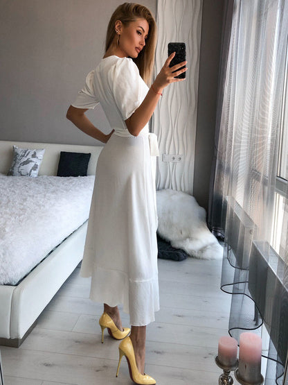 Woman in a white dress taking a mirror selfie in a modern bedroom.