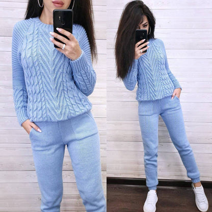 Woman wearing a light blue cable knit sweater and pants, taking a mirror selfie.