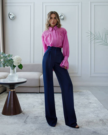 Woman wearing a pink blouse and navy pants in a living room setting.