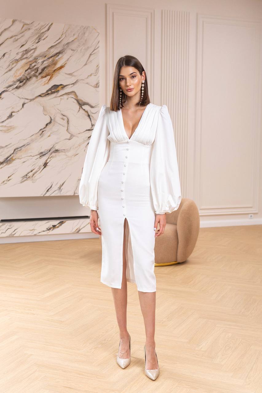 Woman in a white outfit standing in a room with marble wall and wooden floor.