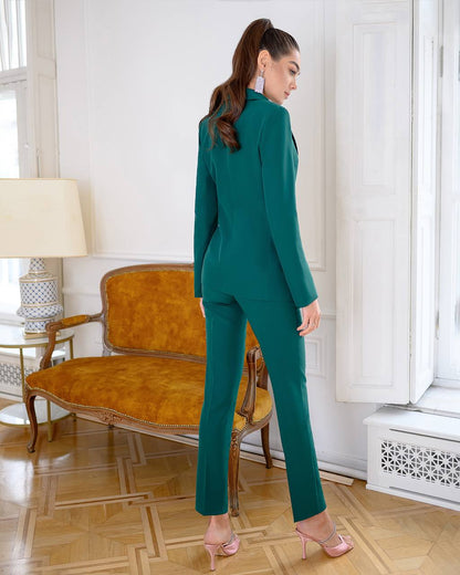 Woman in a teal suit standing in a room with a vintage chair and lamp.