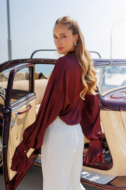 Woman in a burgundy top and white skirt standing next to an open-top vintage car.