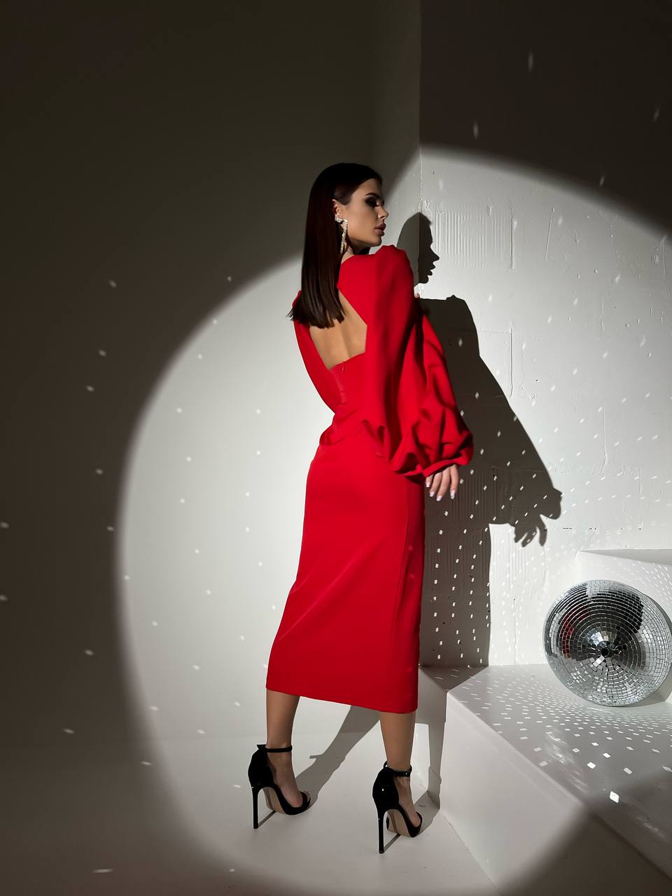 Woman in a red dress standing in a spotlight with a disco ball in the background