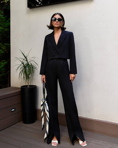 Woman in a black suit standing outdoors with a plant and wooden bench in the background