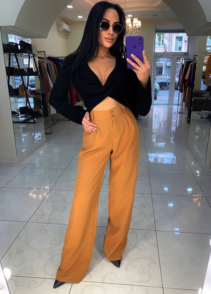 Woman taking a mirror selfie wearing a black top and mustard yellow pants in a store.