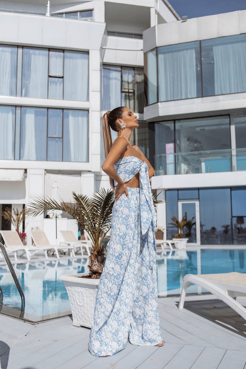 Woman in a blue floral dress standing in front of a modern building with a pool.
