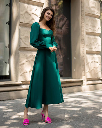 Woman in a green dress with pink shoes standing on a street.
