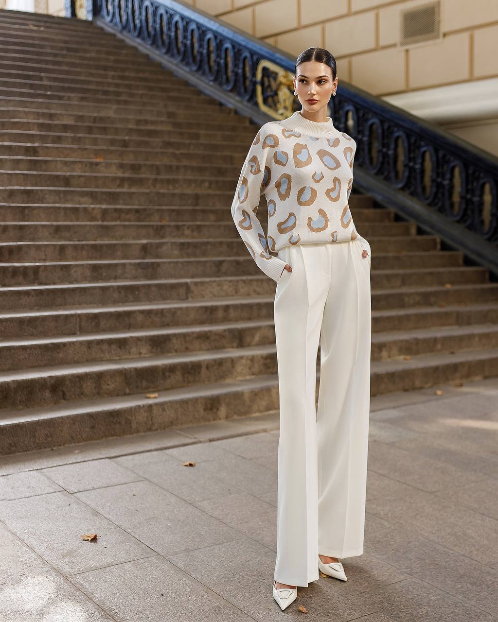 Woman in a patterned sweater and white pants standing on steps outdoors