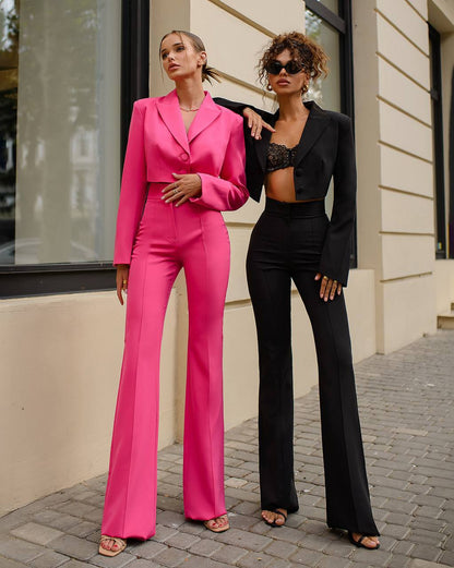Two women in pink and black suits standing on a street.