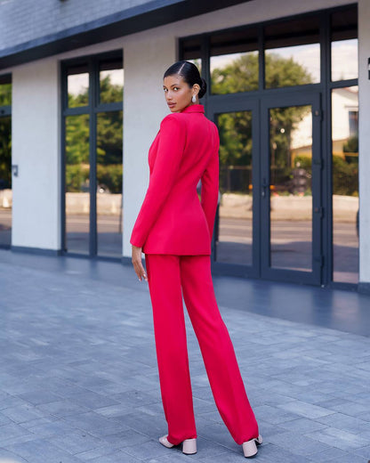 Woman in a bright pink suit standing in front of a modern building.