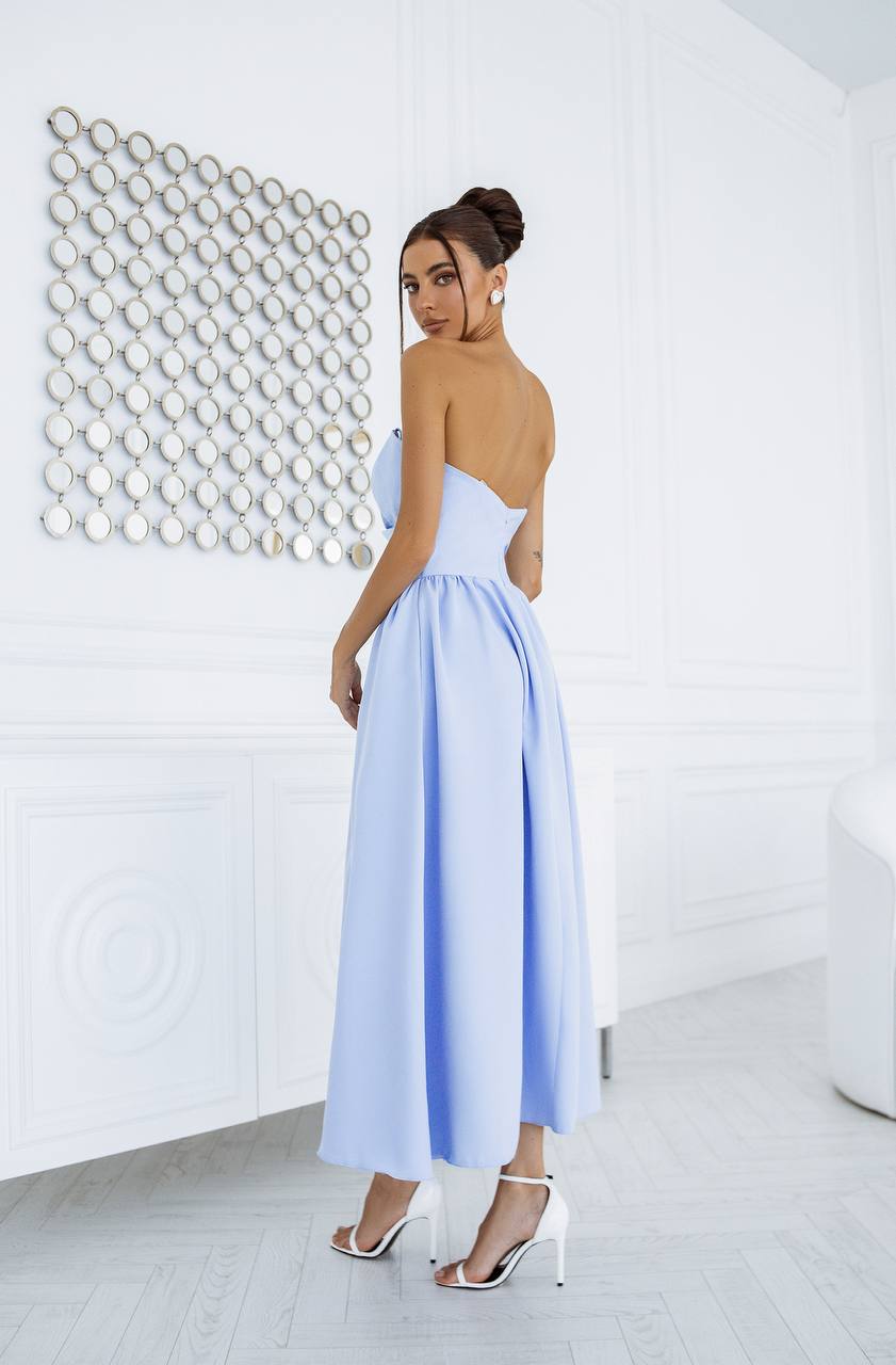 Woman wearing a light blue dress with cut-out design in a minimalistic room.