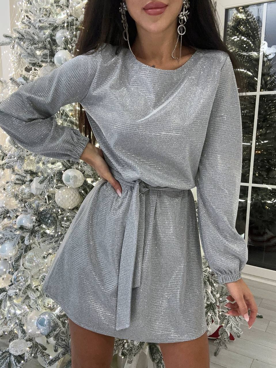 Woman wearing a silver glittery dress in front of a decorated Christmas tree.