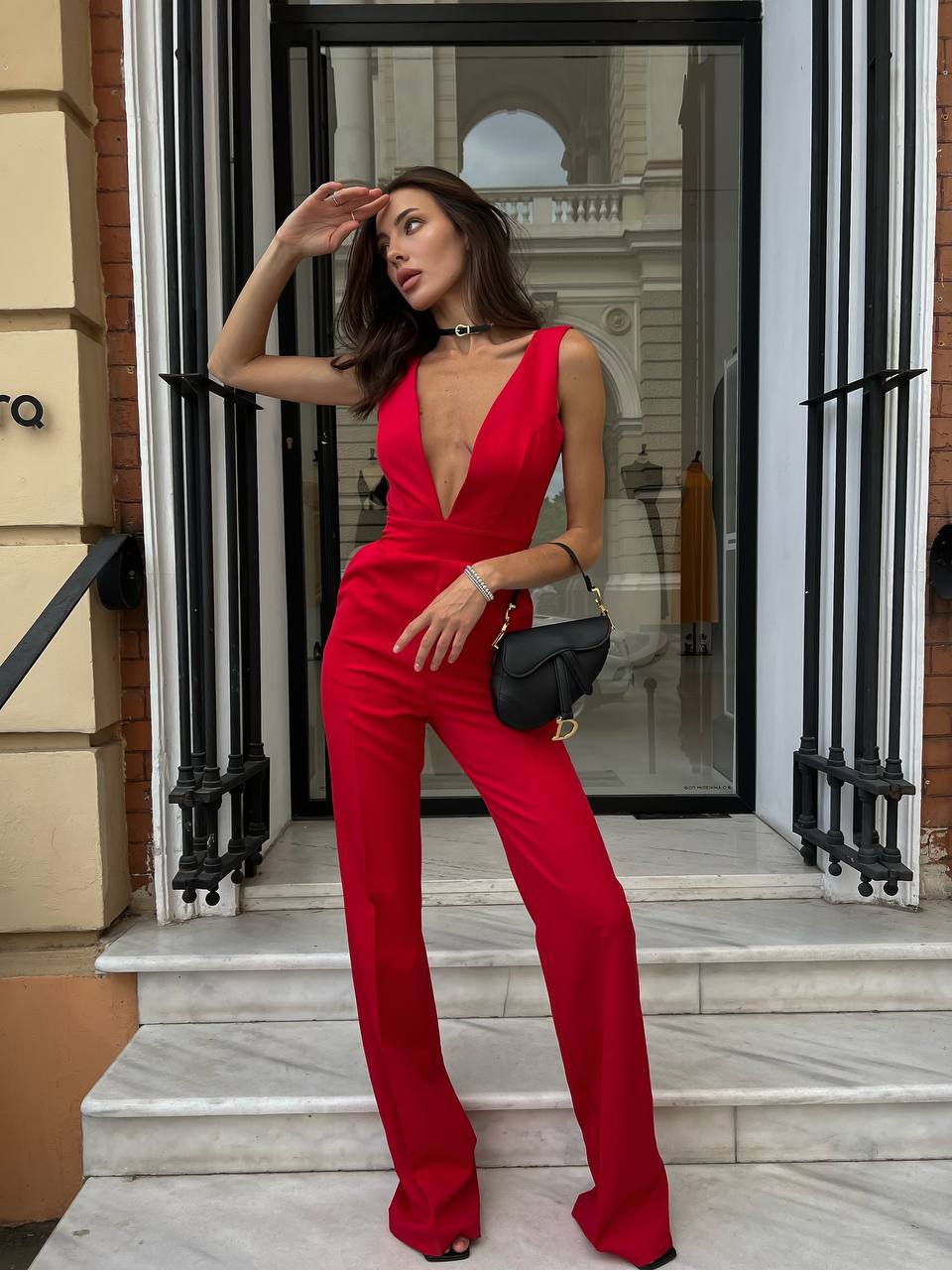Woman in a red jumpsuit standing in front of a building entrance.