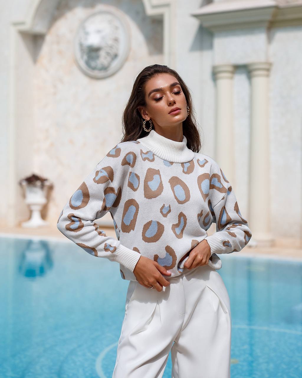 Woman wearing a patterned sweater by a pool with classical architecture in the background