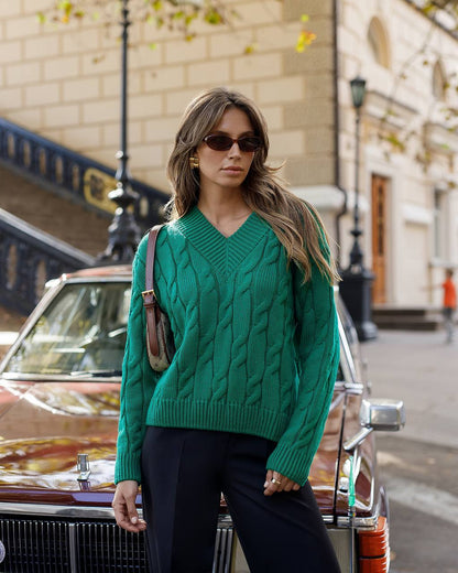Woman in a green sweater standing next to a vintage car on a city street.