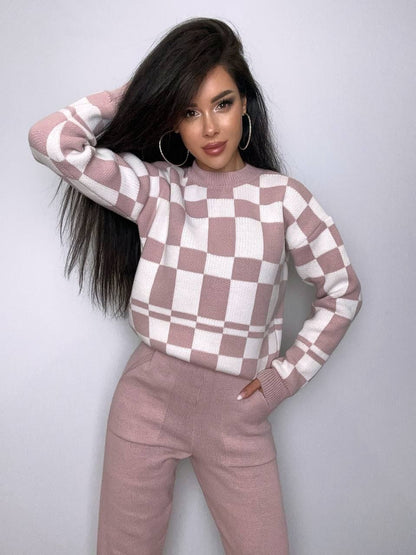 Woman wearing a checkered pink and white sweater and pants against a plain background