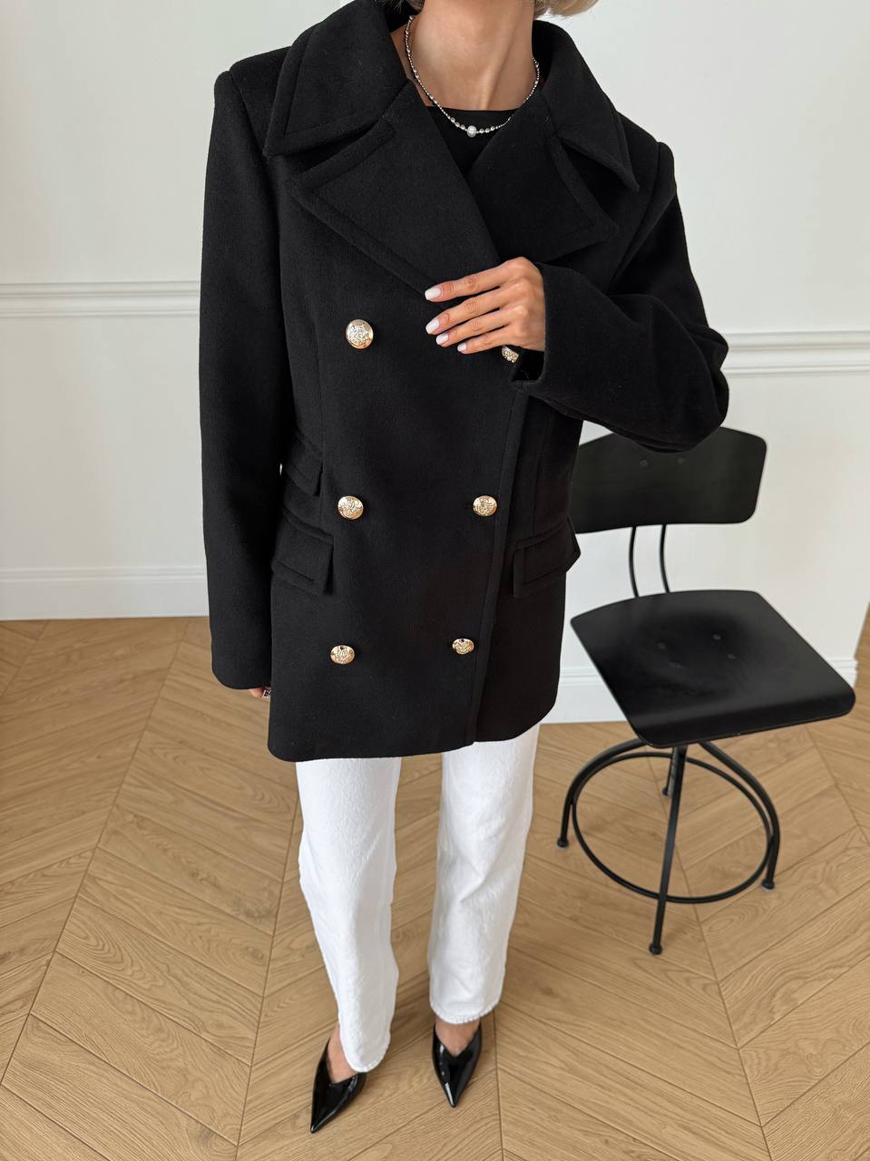 Person wearing a black coat with gold buttons in an indoor setting.