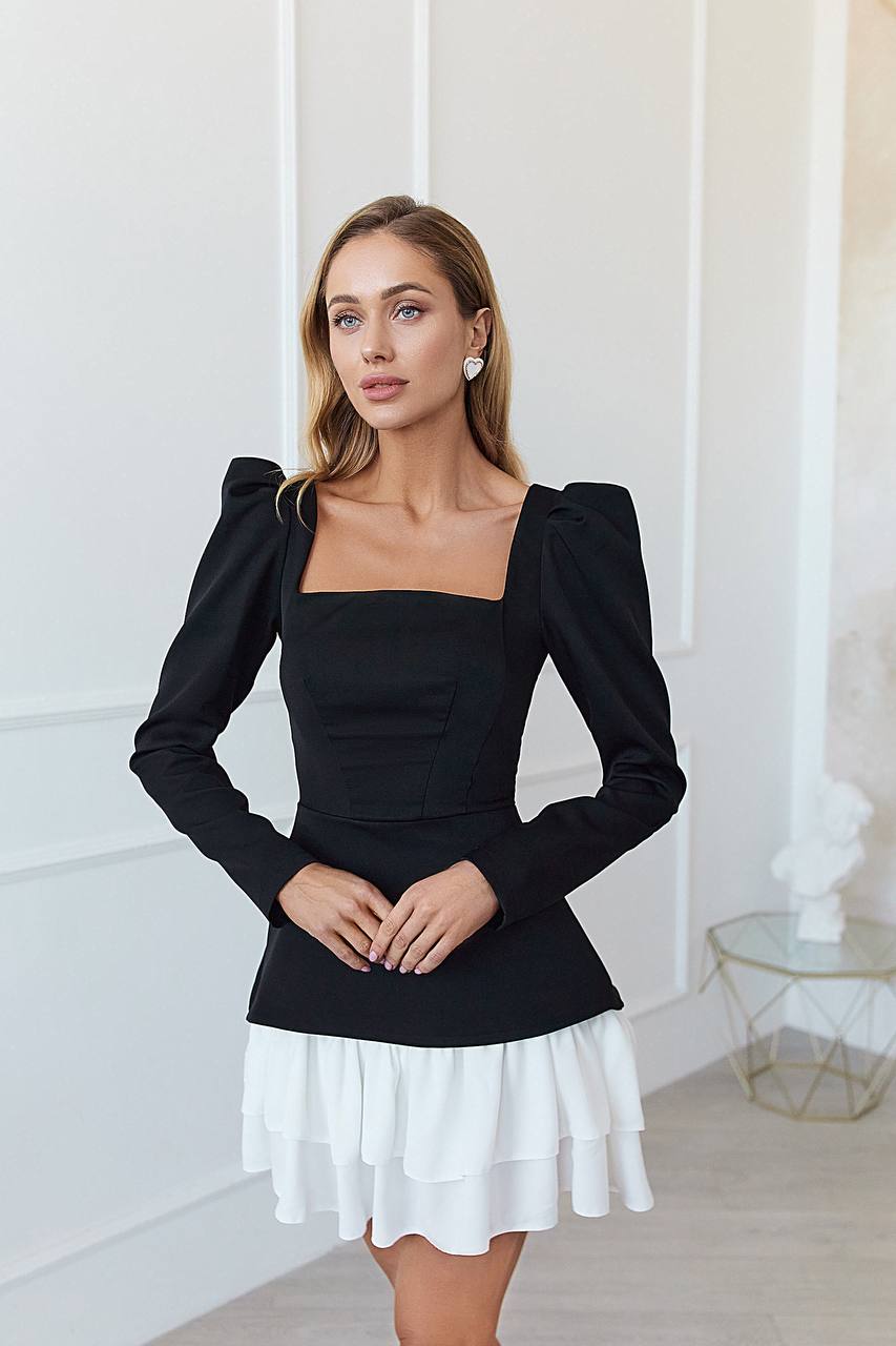 Woman wearing a black top with puffed sleeves and a white skirt in a bright room.