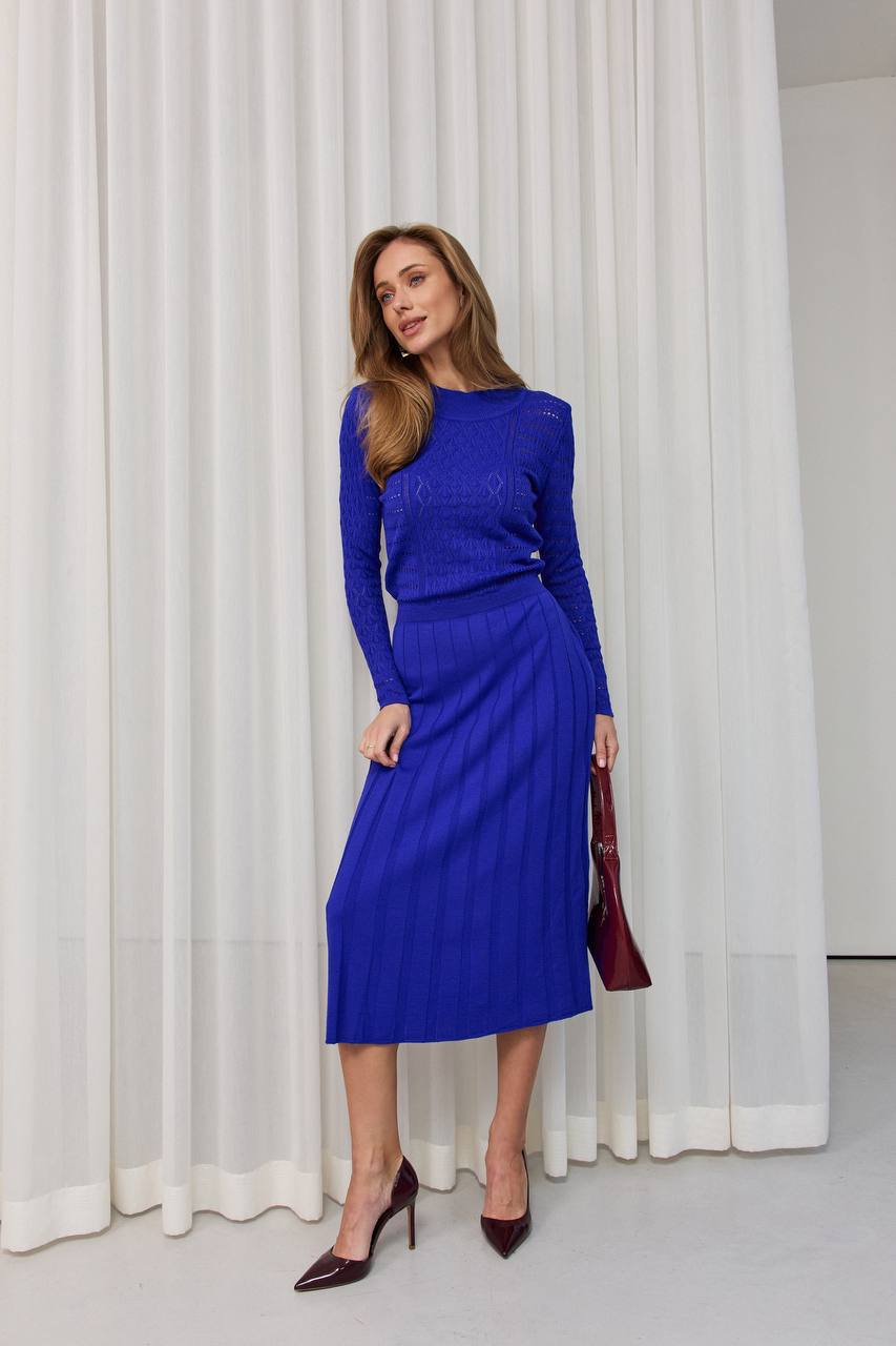 Woman wearing a blue outfit standing in front of white curtains