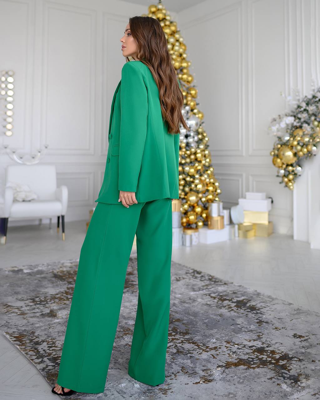 Woman in a green suit standing in a decorated room with Christmas trees.