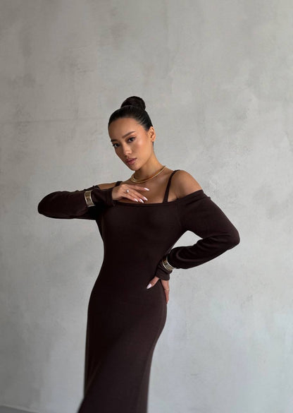 Woman in a dark brown off-shoulder dress posing against a plain background