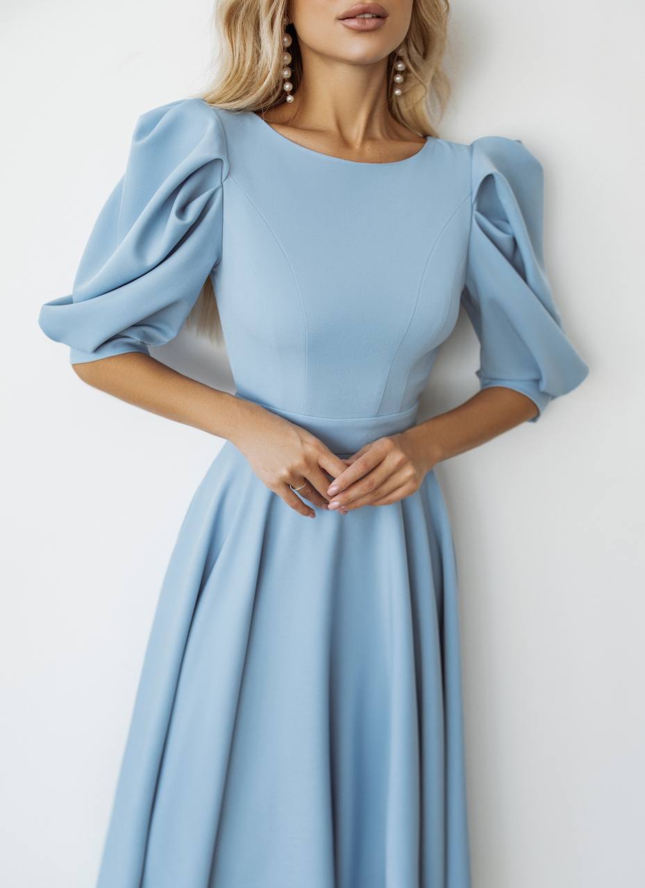 Woman wearing a light blue dress with puffed sleeves against a white background